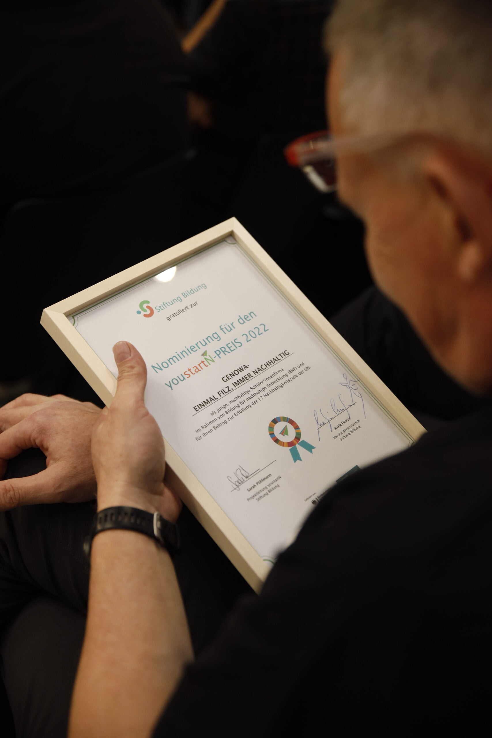 Foto: Sagithjan Surenda, [Blick eines Mannes auf die Nominiertenurkunde der Schulfirma beim youstartN-Preis 2022].