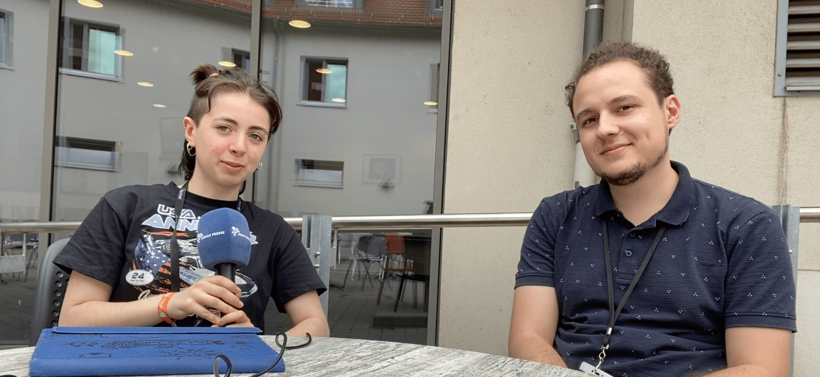 Jadon und Erdal sitzen an einem Tisch und blicken in die Kamera