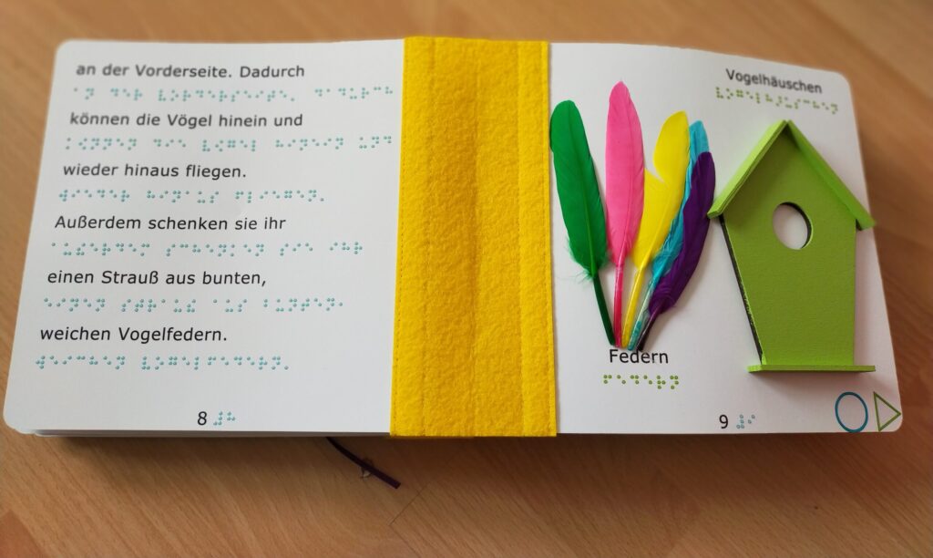 aufgeschlagenes Fühlbuch mit Brauille-Schrift, Federn und Vogelhäuschen