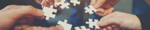 sieben einzelne Hände kommen kreisförmig zusammen, in jeder Hand befindet sich ein weißes Puzzleteil