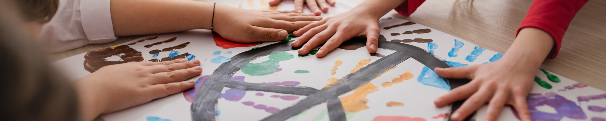 mehrere Kinderhände liegen auf einem Plakat mit bunten Kinderhandabdrücken und einem schwarzen, gemalten Peacezeichen - Slide