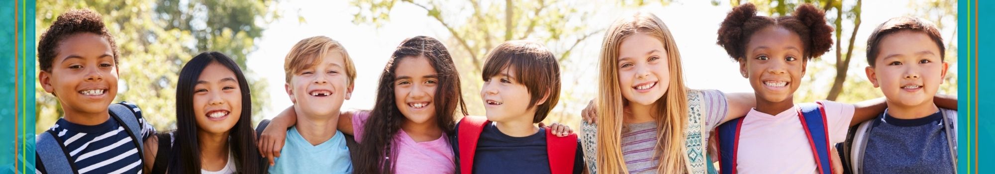 Acht Grundschulkinder stehen in einer Reihe, Arme eingehakt, und lächeln dirket in die Kamera