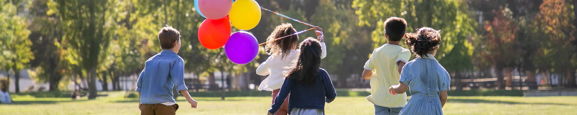 Kinder laufen in einem Park mit Luftballons - Motivbild für den Beitrag 'Klimaschutz ist ein Kinderrecht' -Slide